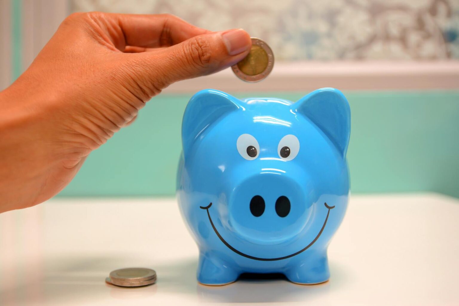 photo by maitree rimthong Hand inserting a coin into a blue piggy bank for savings and money management.